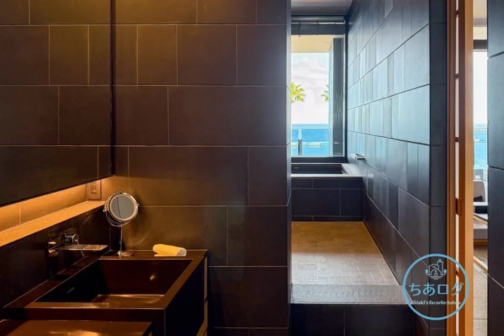 熱海パールスターホテル客室の洗面所から浴室への視点。ダブルボウルの洗面台と、その奥に広がるオーシャンビューのビューバスエリア。