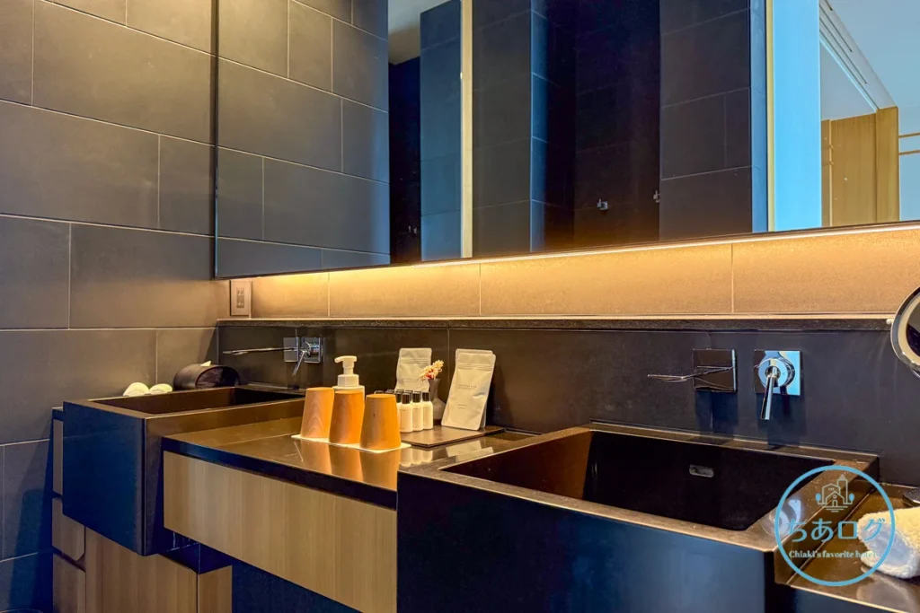 熱海パールスターホテル客室のダブルボウルパウダールーム（洗面所）。大きな鏡、間接照明、NEMOHAMOなどのアメニティが並ぶ。