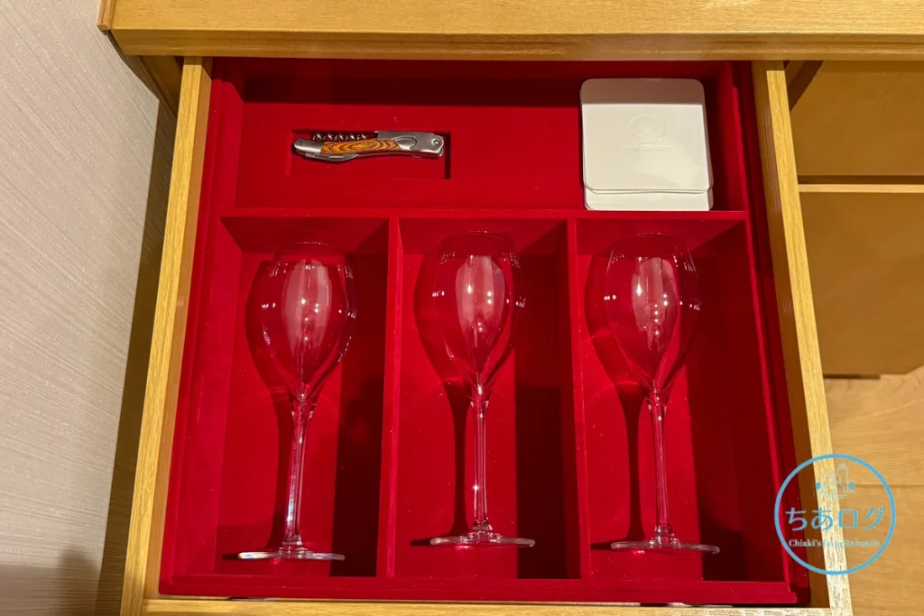 熱海パールスターホテルの引き出しに収められたチューリップ型のシャンパングラス、ソムリエナイフ、およびホテルロゴ入りの高級コースター。