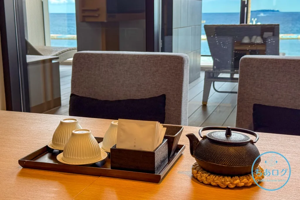 熱海パールスターホテルのリビングテーブルに用意された、南部鉄器の急須としのぎデザインの湯呑み、熱海名物「ぐり茶」のティーセット。背景には熱海の海が広がる。
